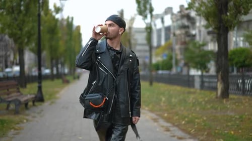 Dolly Shot of Confident Positive Gay Man Strolling on Summer Autumn Alley in City Drinking Coffee