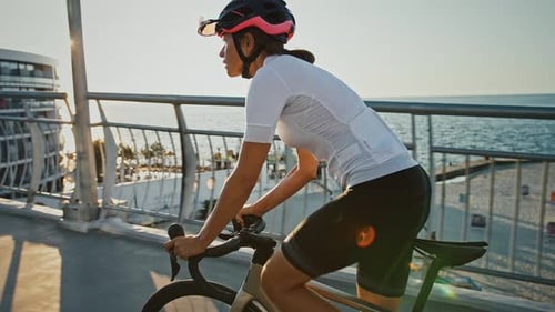 Sportswoman in Protective Helmet is Riding Her Bicycle Uphill Along Bridge Surrounded By City