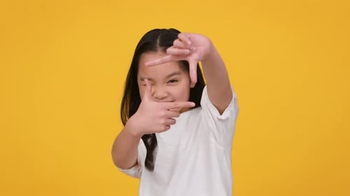 Smiling Girl Makes Finger Frame on Yellow Background