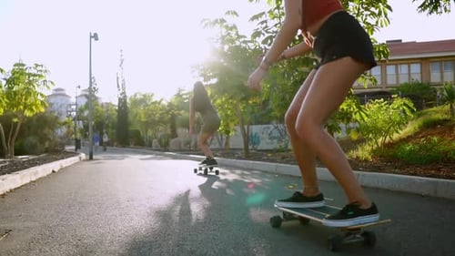Two Female Friends on Skateboards Rides Downhill at the Resort Having Fun Moving and Smiling. Road
