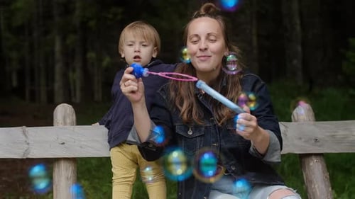 Positiv Junge Frau mit ihren Söhnen spielt mit Seifenblasen und genießt Urlaub im Park.