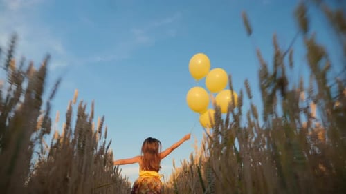Young Girl Runs with Balloons in the Wheat Field