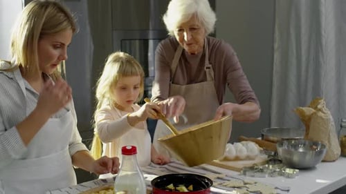 Mutter und Großmutter kochen Apfelkuchen mit kleinem Mädchen