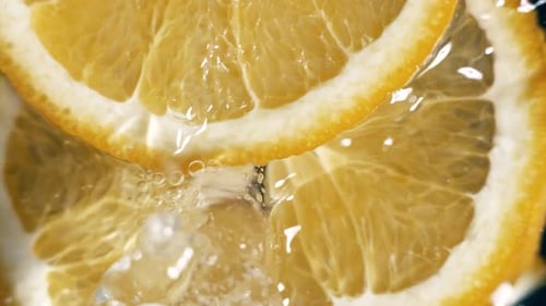 Orangenscheiben fallen in Zeitlupe ins Wasser