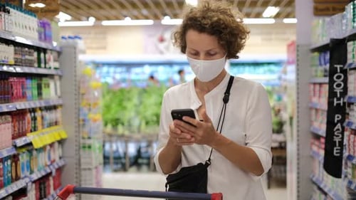 Female Customer Texting Message in a Smartphone While Shopping in Nonfood Supplies Department in the
