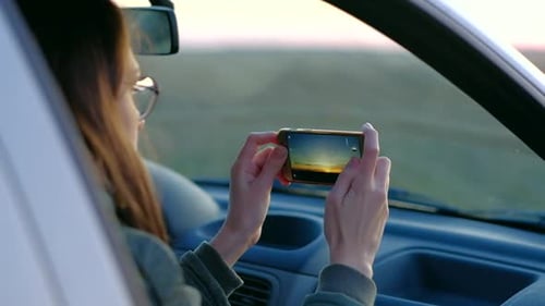 Mädchen mit Brille fotografiert Sonnenuntergang aus dem Auto
