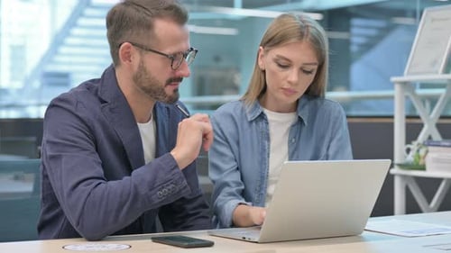 Businessman and Businesswoman Having Discussion on Laptop in Office
