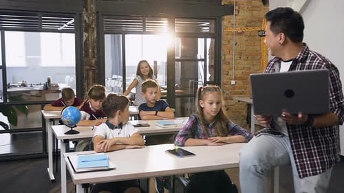 School Children Sitting at Desks Listening and Putting up Hands to Answer Questions