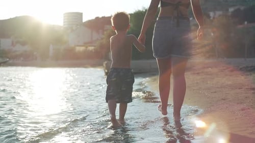 Mom Holds Her Son's Hand and They Walk Along the Seashore