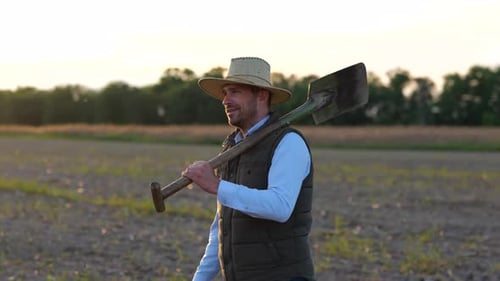 Portrait of Happy Caucasian Man Farmer Walks Across Field Carrying Shovel on Shoulder