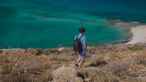 A Guy a Tourist with a Backpack Goes Down the Slope to the Beautiful Mediterranean Sea