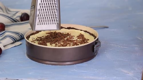 Woman chef holds metal grater and grates chocolate dough. Making chocolate pie.