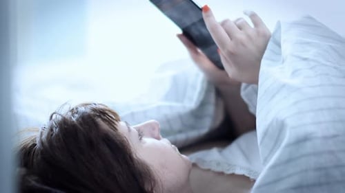 Woman Relaxes in Bed with Smartphone