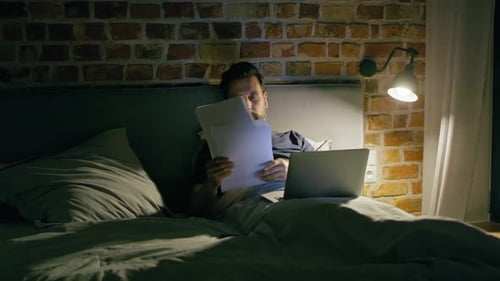 Man Works on Laptop in Bed at Night