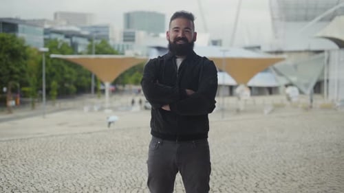 Man smiling with beard, crossing arms in city