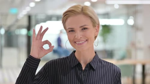 Woman Smiles and Gives Okay Gesture in Office