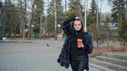 Beautiful young girl in luxury fur coat in the city park