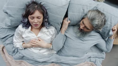 Jeune femme ronflant pendant son sommeil alors que son mari irrité couvre la tête avec un oreiller