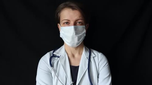 Porträt einer traurigen Ärztin in einer Maske auf schwarzem Hintergrund.