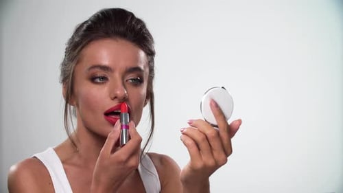 Woman Applies Red Lipstick Looking into Mirror