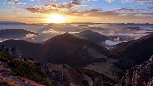 Sunrise in a mountain landscape. The clouds are painted in warm colors. Low clouds spill over the hi