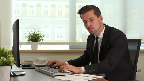 An office worker in a suit works on a computer and reads papers for work
