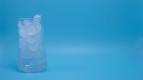 Ice Melting in Glass on Light Blue Background
