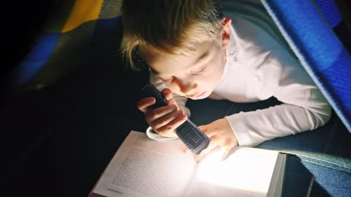 Child Reading with Flashlight Under Blanket