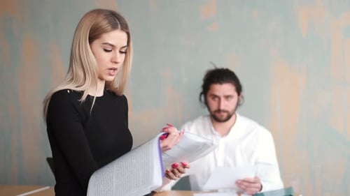 Young Woman Office Worker Close Up Work with Papers and Her Male Collegue at the Background