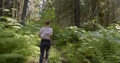 Following Female Running on Forest Footpath in Wilderness of Alaska, Slow Motion