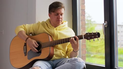 Man Plays Acoustic Guitar by Bright Window