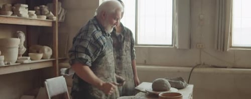 Senior Potter Teaching Young Woman to Throw on Wheel