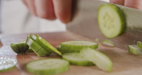 Macro shot of a large chef knife slicing a cucumber