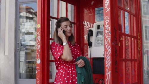 Woman Talking on Phone in Red Telephone Booth