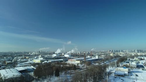 Factory buildings covered with snow. Factory smoke chimneys. There is a railway nearby