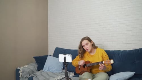 Una mujer aprende a tocar el ukelele viendo un vídeo tutorial en el teléfono