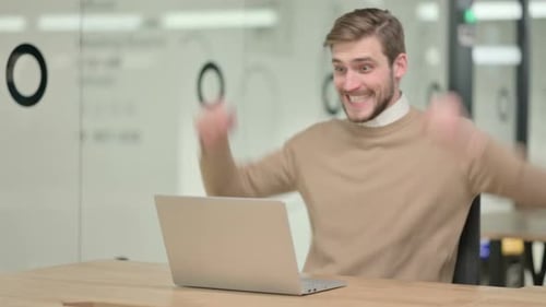 Creative Young Man with Laptop Celebrating in Office