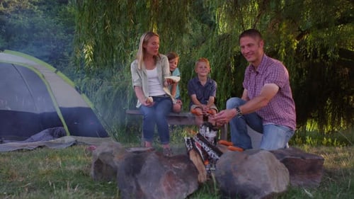 Family roasting hot dogs at camp site