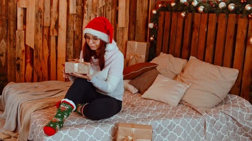 Woman in Santa Hat Opening Christmas Gift on Bed