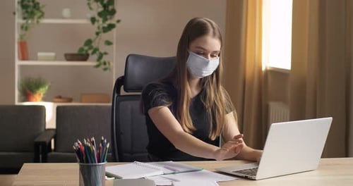 Woman Working at Desk Wearing Mask and Using Laptop