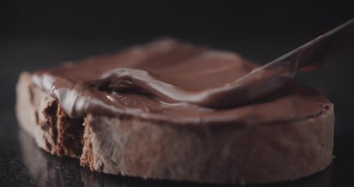 Spreading chocolate cream on a slice of rye bread.
Pastry close up shot.