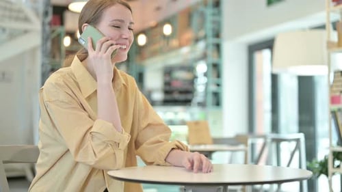 Cheerful Young Woman Talking on Smartphone in Cafe