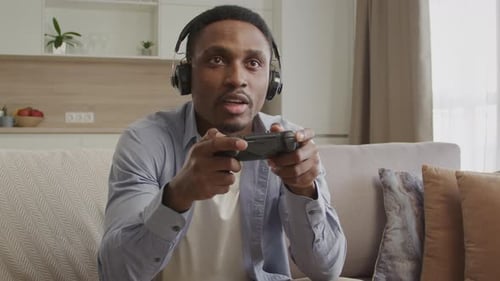 Man Plays Video Game with Controller and Headphones
