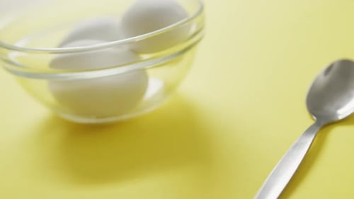 Video of close up of glass bowl with eggs on yellow background