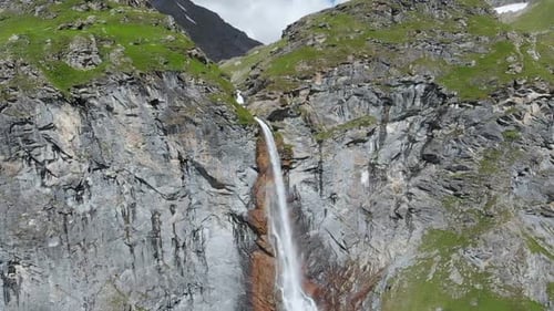 Aerial slow motion: drone flying over scenic high waterfall, mountain stream falling from cliff