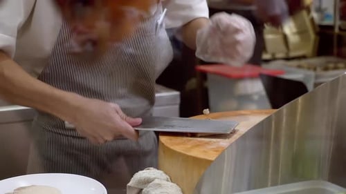 Der Küchenchef nimmt das Brathähnchen und hackt es mit einem Hackmesser auf einem Holzbrett