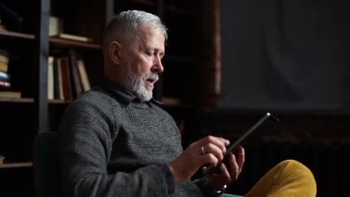 Adult Man Using Tablet Inside Near Bookshelf