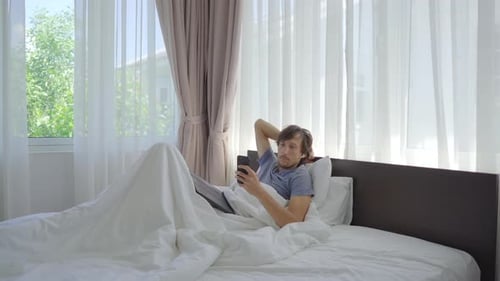 Man Relaxes in Bed Using a Smartphone