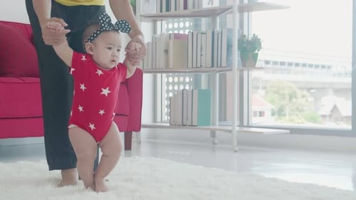 Happy family with mother support baby step walk in the living room at home.