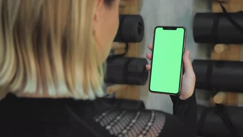 back view of fitness woman using green screen smart phone at home. Woman preparing for workout
